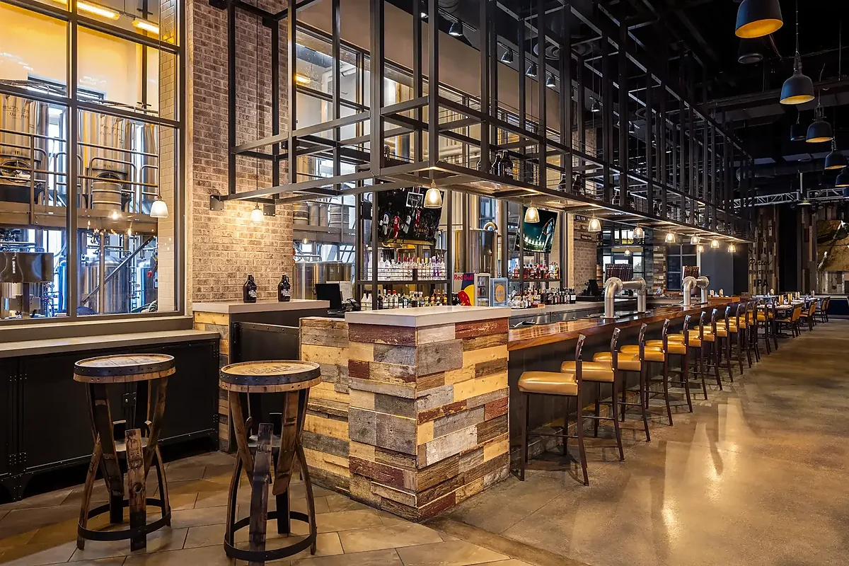 Long bar with stools beside windows into the on-site brewery