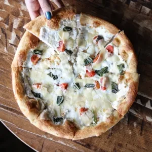 Hand lifting a slice of white pizza with tomatoes and basil.