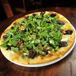 Flatbread topped with arugula, figs, pine nuts, prosciutto, and cheese.