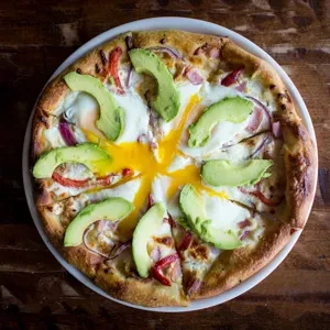 Top-down view of pizza with avocado, runny egg, red onion, and meat.