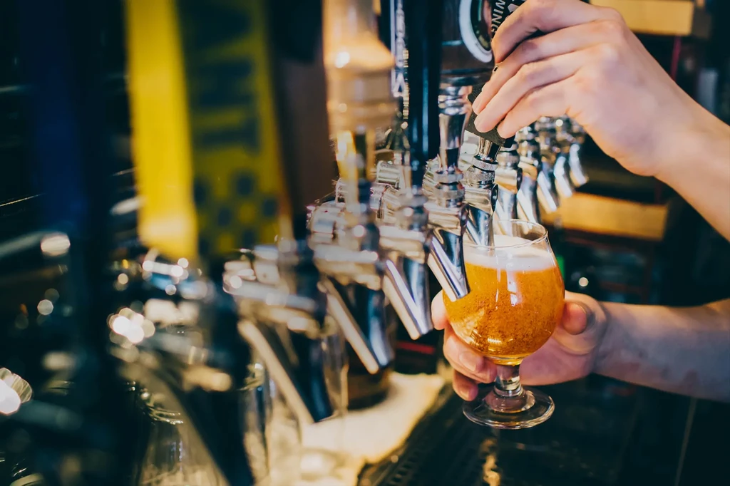 Hands pour golden beer from a tap into a stemmed glass.
