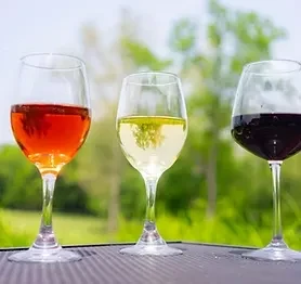 Three wine glasses with rosé, white, and red wine outdoors.