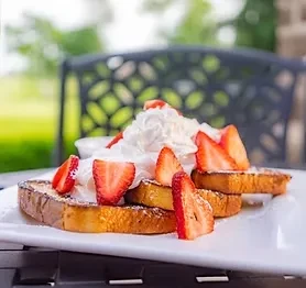 Golden French toast with whipped cream and strawberries, served outdoors.