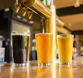 Three glasses of beverages, dark to light, at a taproom.