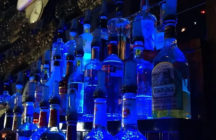 Smirnoff and Yukon Jack bottles glowing blue on a dark bar shelf.