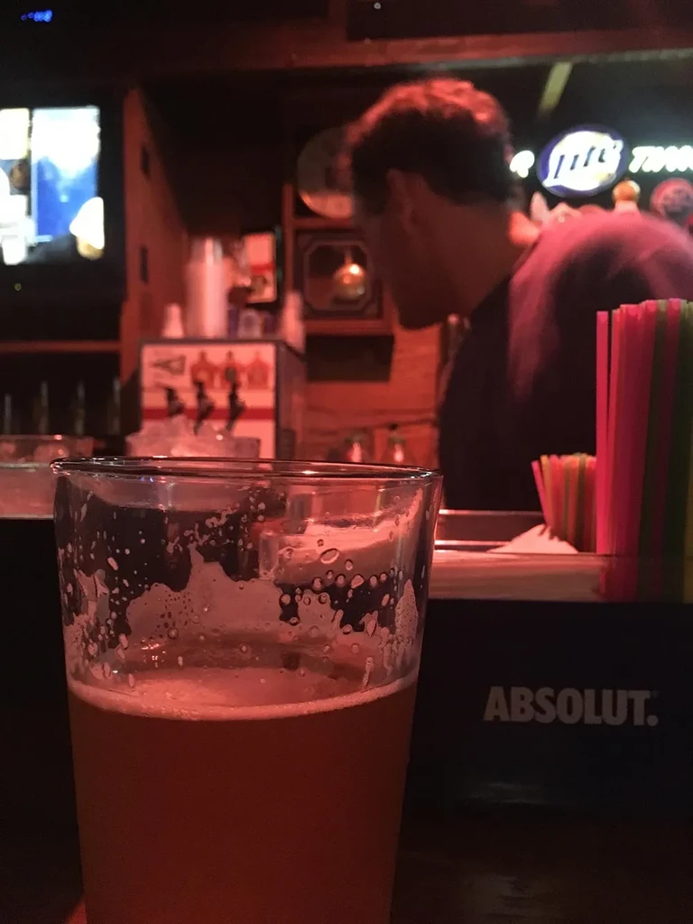 Amber beer, frothy head, ABSOLUT., bartender in dim bar.