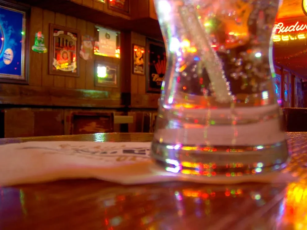Bubbly drink with straw on a bar, reflecting colorful neon lights.
