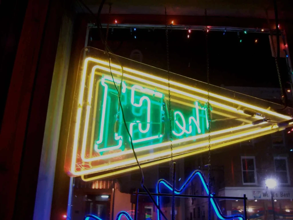 Mirrored yellow and green triangular neon sign in a window.