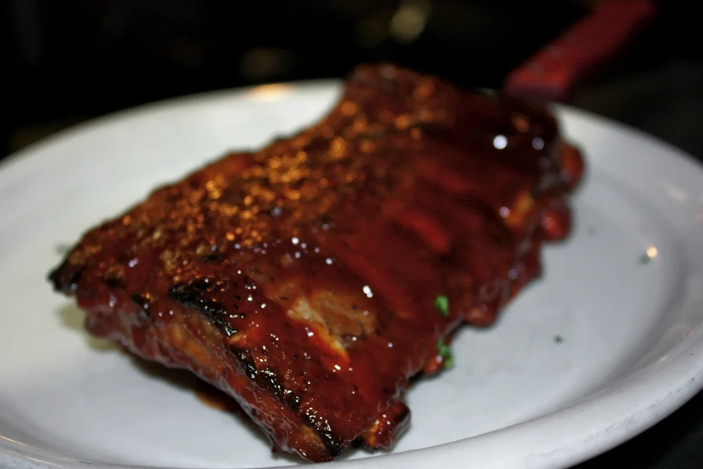 Close-up of barbecued ribs with glossy BBQ sauce and green seasoning.