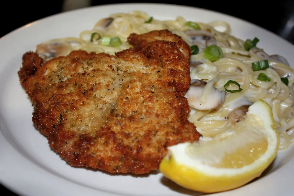 Breaded cutlet, pasta with mushrooms, and a lemon wedge on a plate.