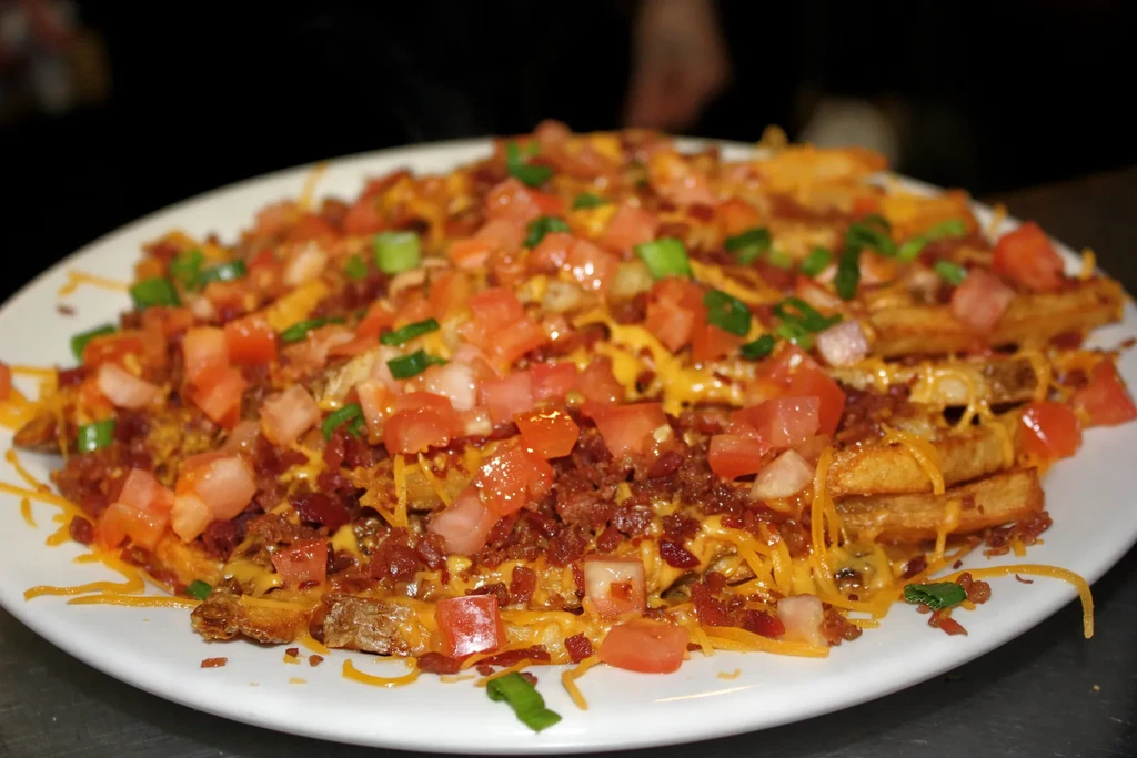 Close-up of loaded fries with cheese, bacon, tomatoes, and scallions.