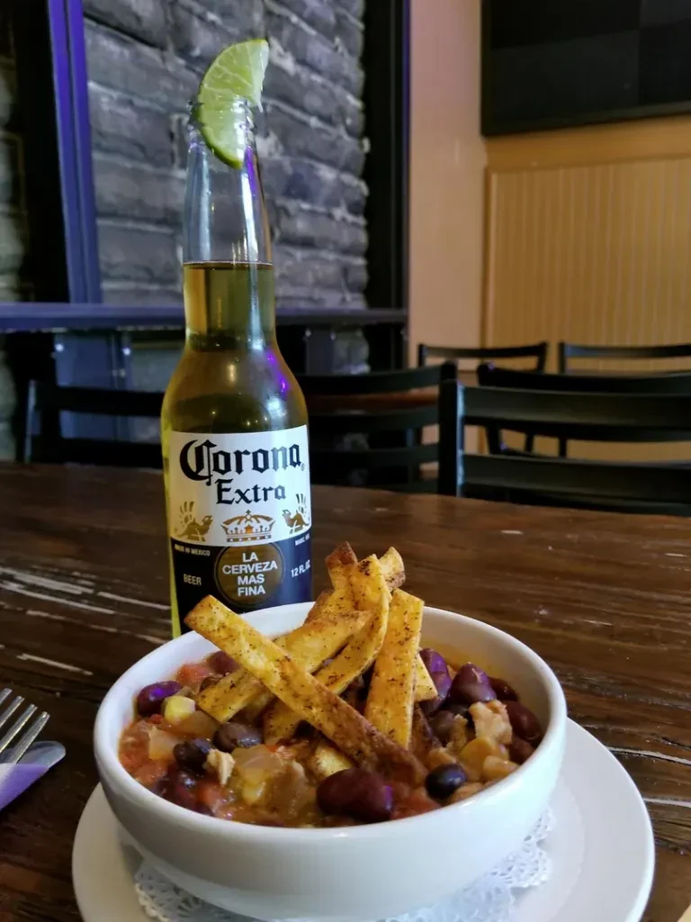 Corona beer with lime next to chili with beans, corn, and strips.