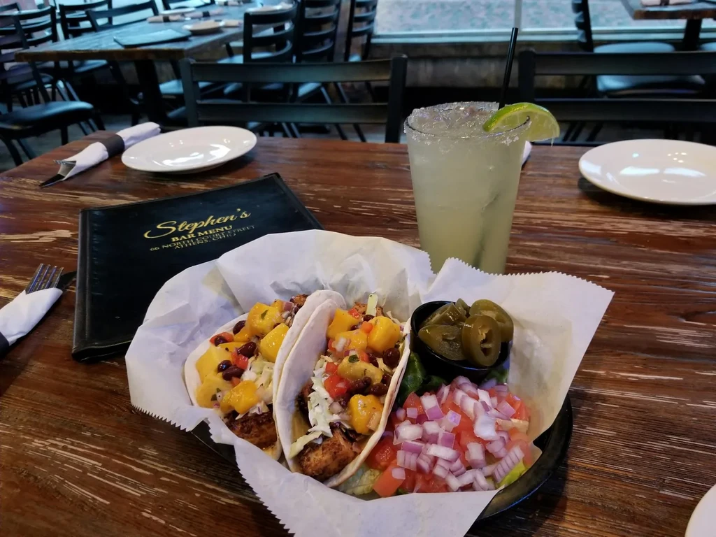 Two colorful tacos, mango salsa, a margarita, and Stephen's bar menu.