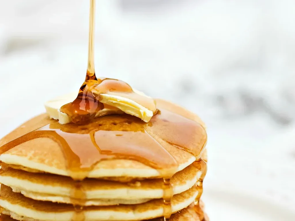 Stack of golden-brown pancakes with melting butter and pouring syrup.