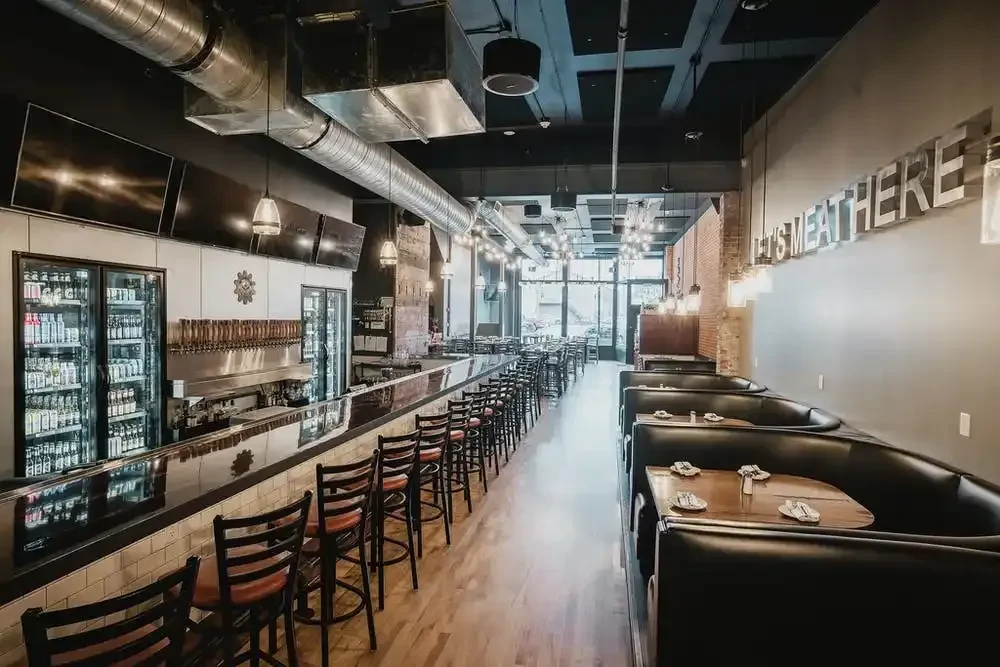 Empty modern restaurant with a long bar, booths, and "IT'S MEAT HERE" sign.