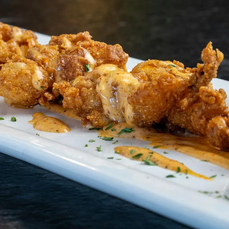 Crispy deep-fried food with orange sauce and fresh herbs on a white plate.