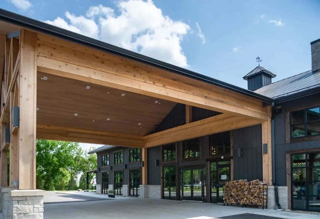 Modern-rustic building, prominent wooden beam entrance, stacked firewood.
