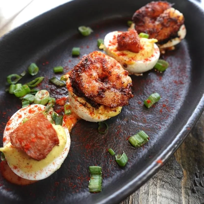 Four deviled eggs with shrimp and crispy meat, garnished with spice.