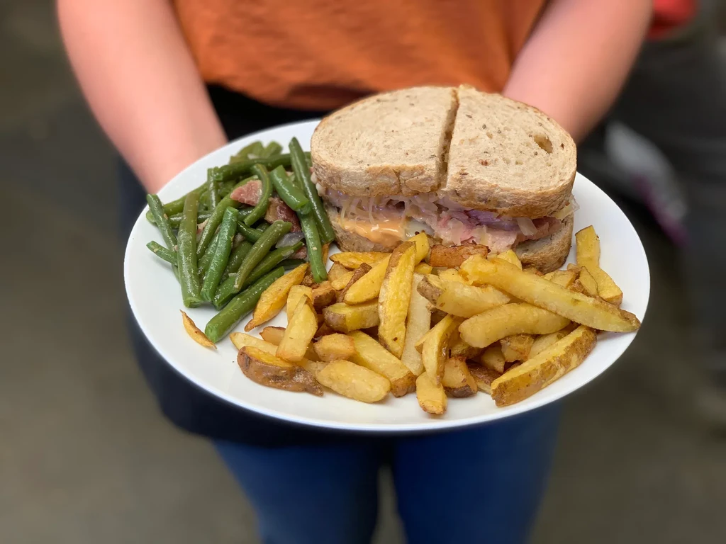 Close-up of a Reuben sandwich, potato wedges, and green beans with bacon.