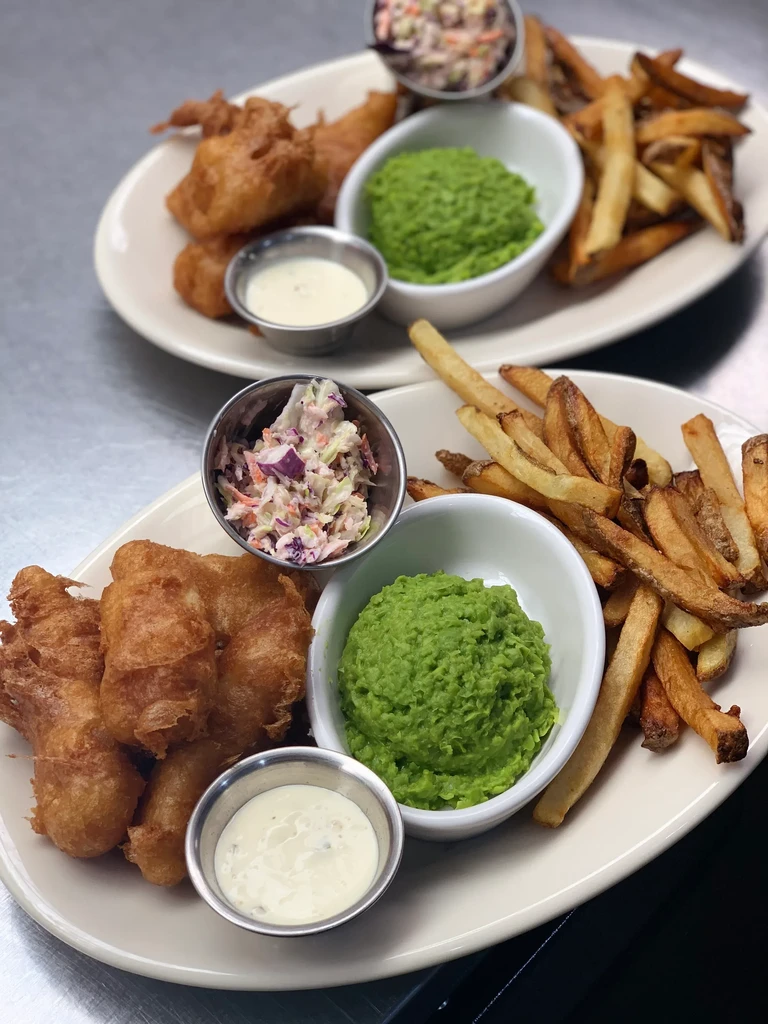 Two plates of classic fish and chips with peas and sauces.