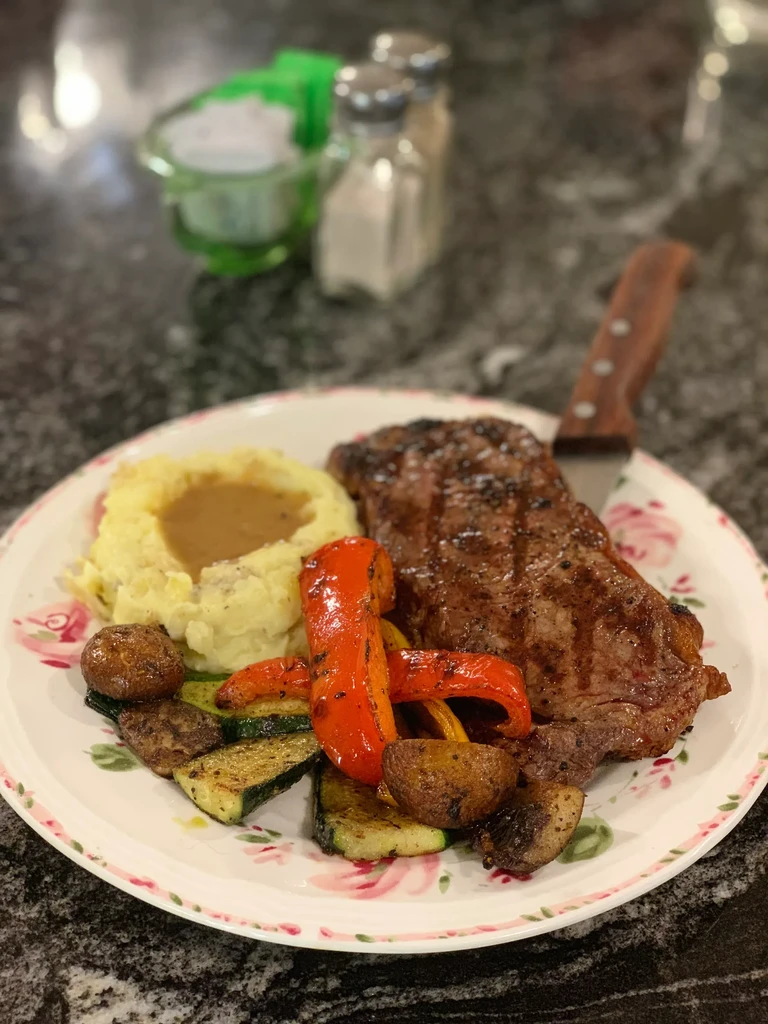 Grilled steak, mashed potatoes, and roasted vegetables on a floral plate.