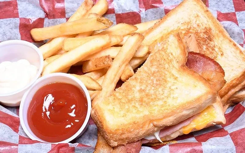 Grilled cheese and bacon sandwich with french fries and sauces.
