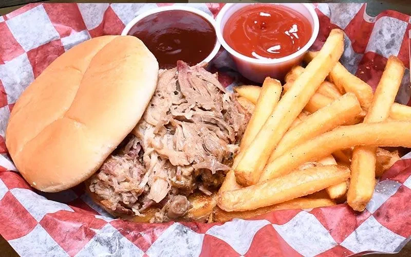 Pulled pork sandwich, fries, BBQ sauce, ketchup in a basket.