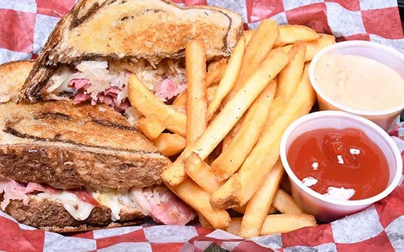 Reuben sandwich, french fries, and sauces served in a checkered basket.