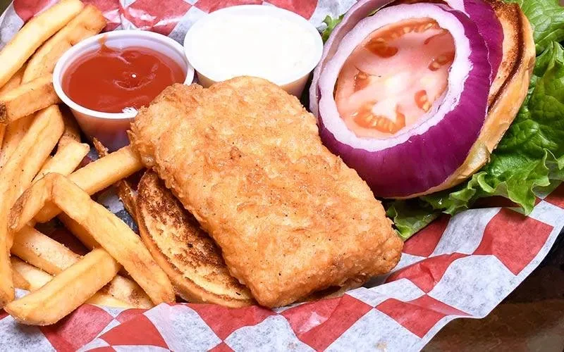 Overhead view of a fried sandwich, fries, ketchup, and tartar sauce.