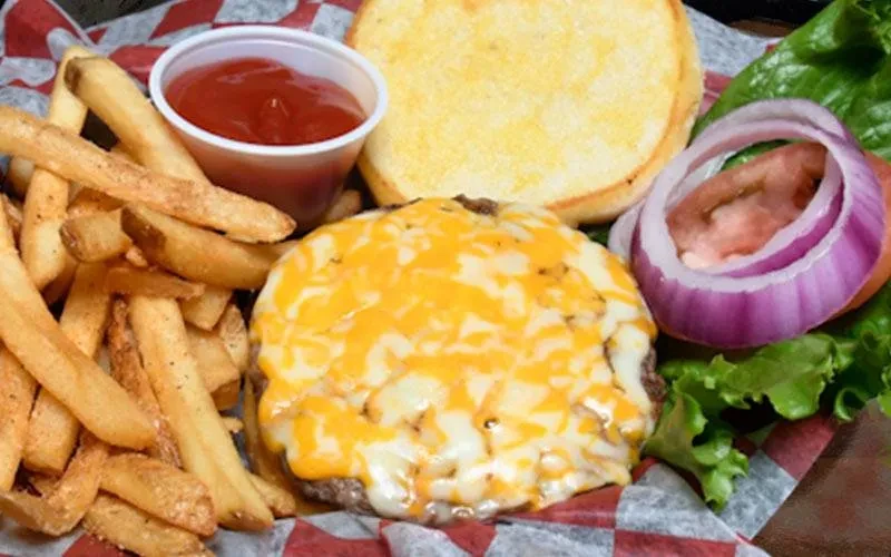 Cheeseburger with melted cheese, fries, and ketchup in a checkered basket.