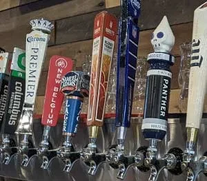 Multiple, varied beer tap handles lined up against a wooden wall.
