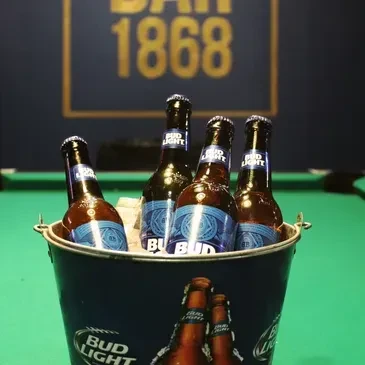 Bud Light bucket of ice and four beers on a pool table.