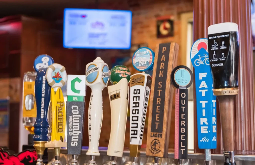 Twelve distinct branded beer tap handles displayed in a bar.