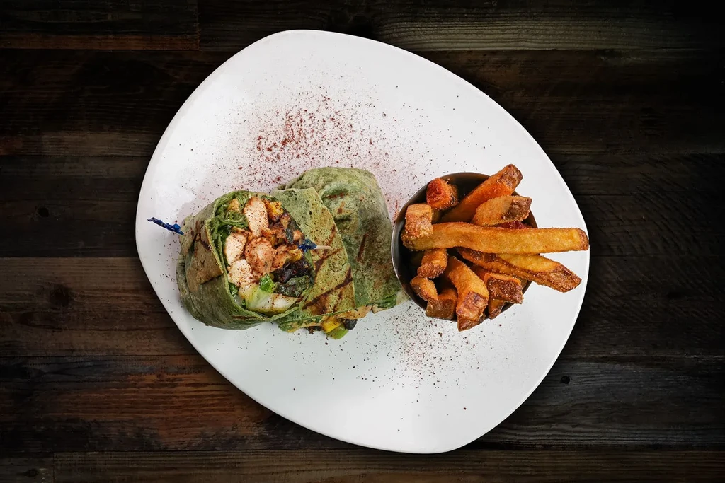 Green chicken wrap, fries, and spices on an irregular white plate.