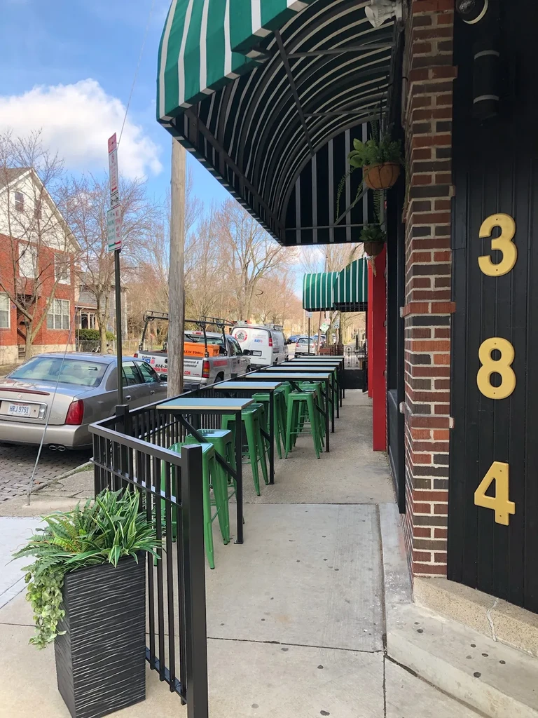 Restaurant exterior with green awning, sunny patio, and '384' sign.