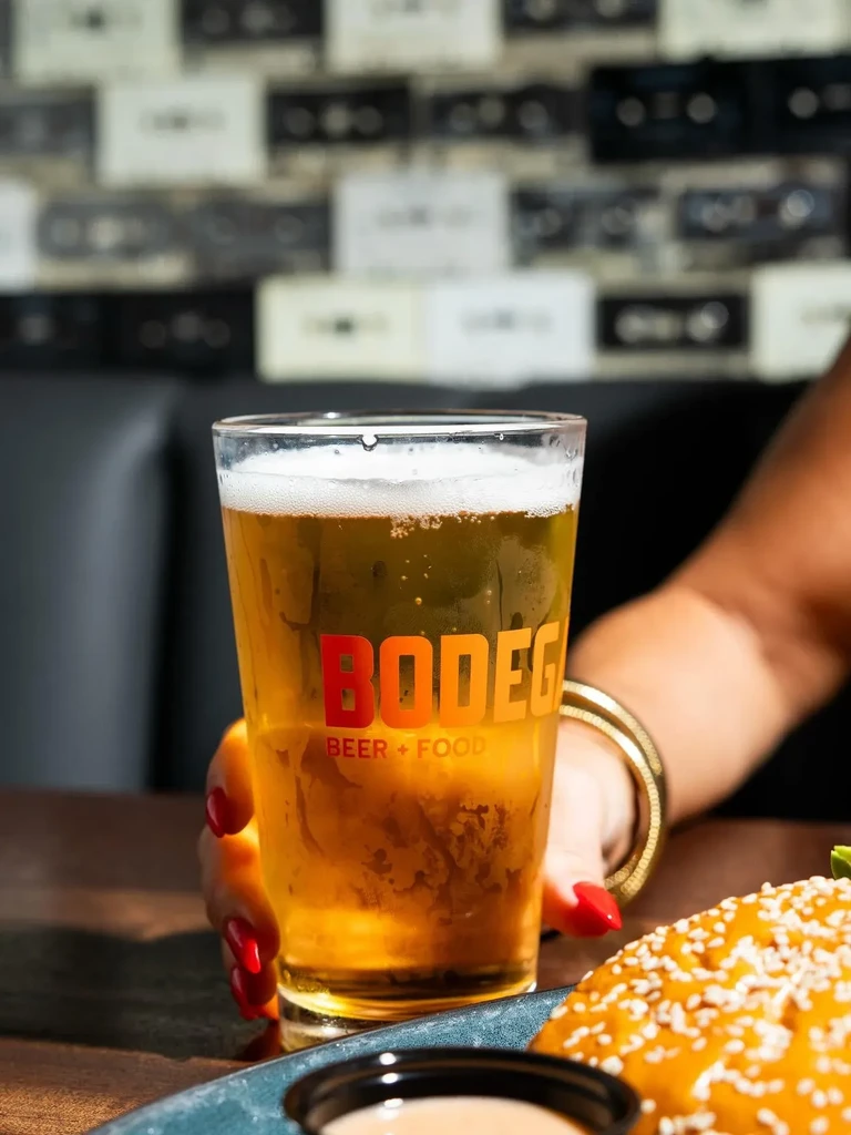 Cold Bodega beer in hand with red nails, burger and sauce.