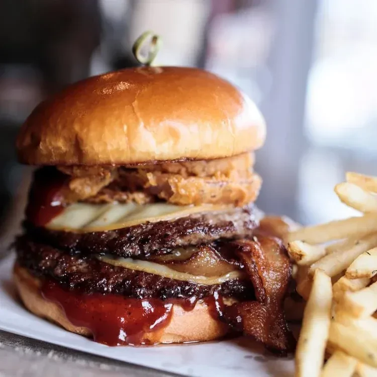 Stacked double cheeseburger with onion rings, bacon, and golden fries.