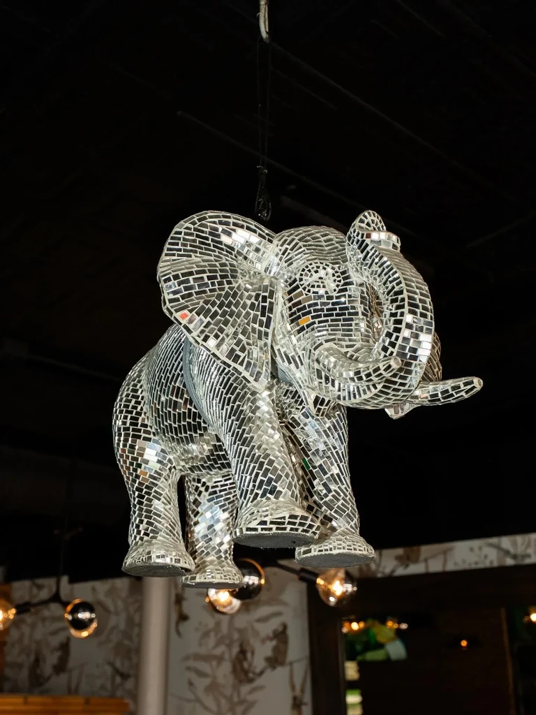 Large, suspended mirrored elephant figure, like a disco ball, reflects light.