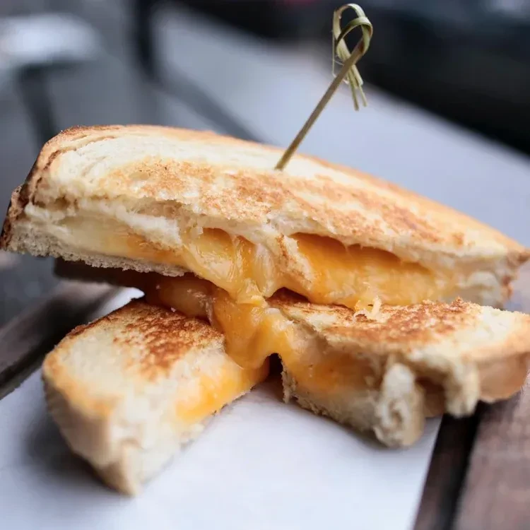 Grilled cheese sandwich cut in half, with gooey melted orange cheese.