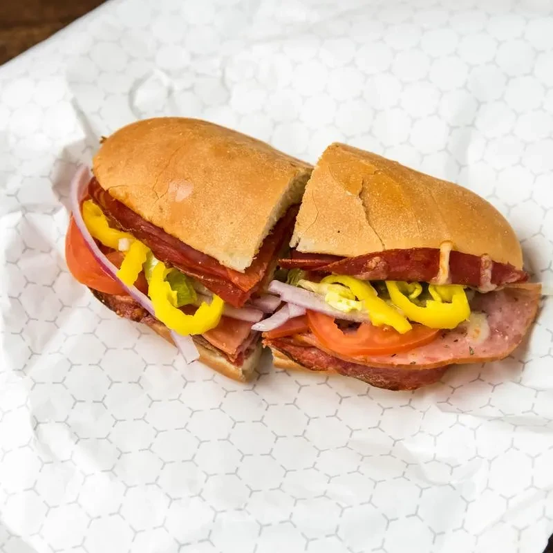 Sub sandwich with deli meats, tomatoes, banana peppers, and onion.