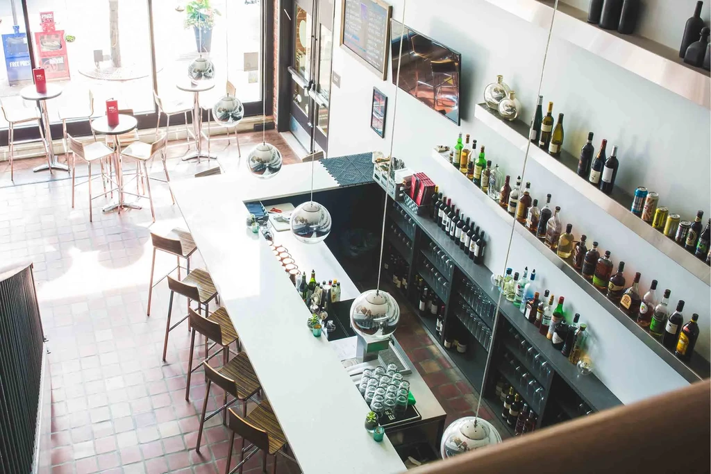 Modern bar interior with a white counter, stocked shelves, and bright windows.