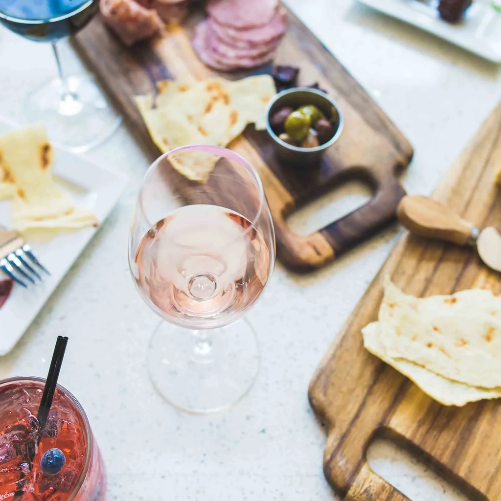 Bright table with charcuterie boards, wines, and a red cocktail.