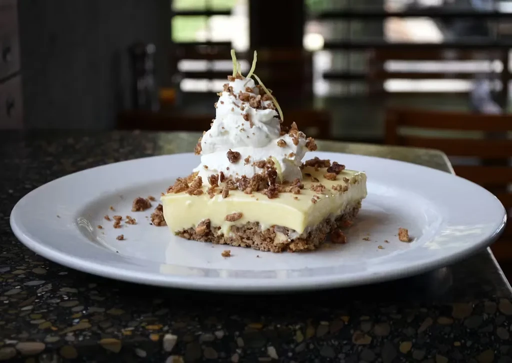 Rectangular dessert with creamy top, crumb base, whipped cream, and zest.