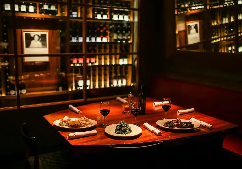 Dimly lit restaurant table set with food, wine, and a wine rack.