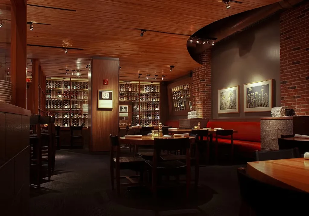 Upscale restaurant dining area with warm wood, brick, and wine bottles.