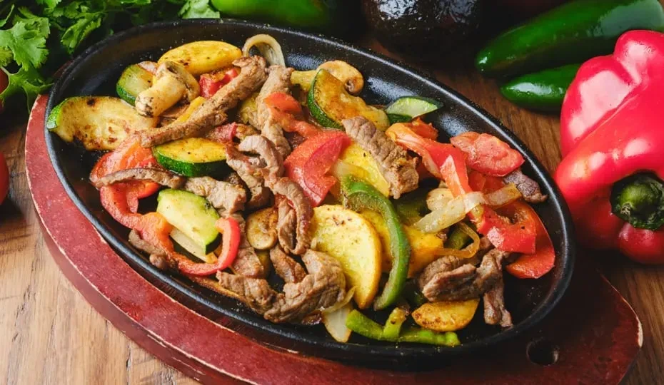 Sizzling fajita platter with beef, colorful vegetables, and mushrooms.