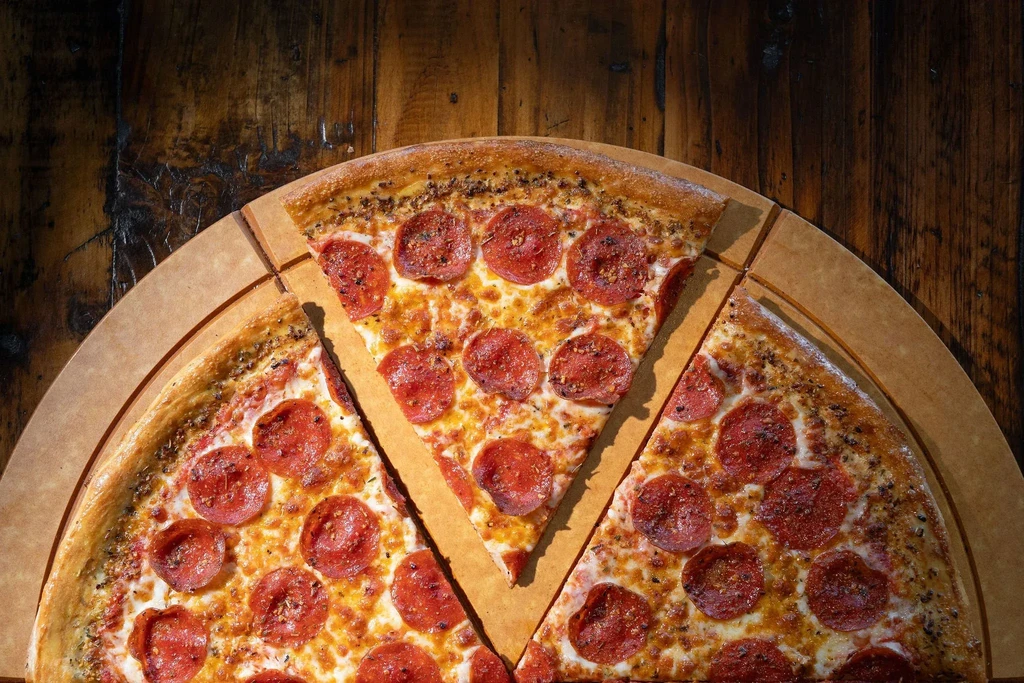 Partially cut pepperoni pizza with a separated slice on wood.
