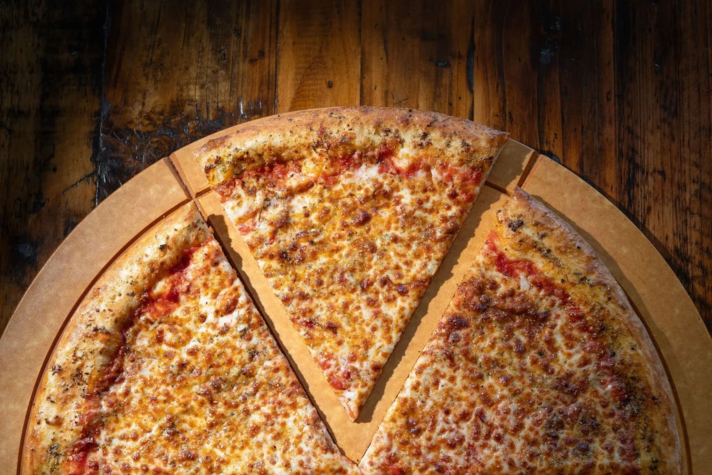 Top-down of cut cheese pizza on tray and wooden table.