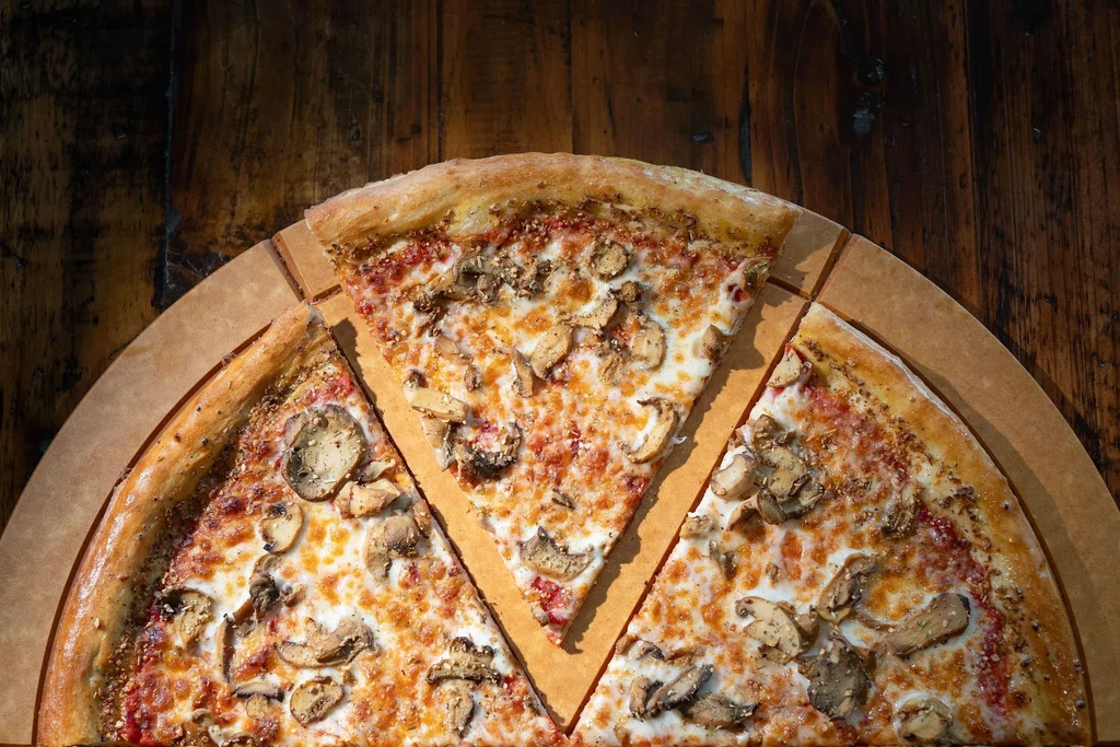 Overhead view: Freshly baked mushroom pizza on wooden table, slice removed.
