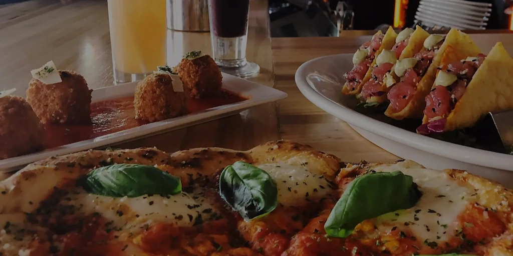 Close-up of rustic pizza, arancini, and tuna tacos on a table.